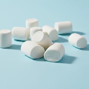 A pile of fluffy white allergy-free vegan marshmallows scattered on a light blue background.